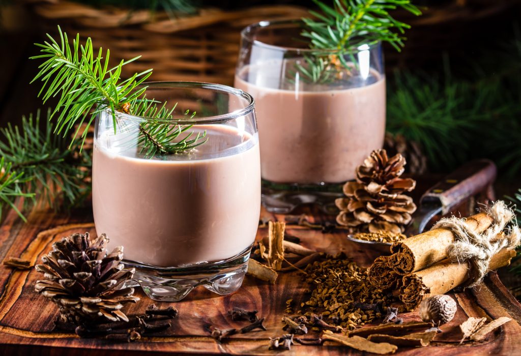 Traditional chilean alcohol Christmas drink Cola de mono - momkey tail with milk, aguardiente, cofee and spices on wooden board decorated fir tree brunches